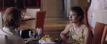 Movie still from “Stars at Noon” (2022), directed by Claire Denis – A woman sitting at a table with a plate of food in front of her; Medium shot, Over the shoulder angle