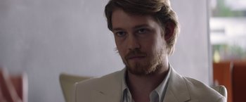 Movie still from “Stars at Noon” (2022), directed by Claire Denis – A person wearing a suit and beard; Close Up shot, Over the shoulder angle