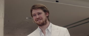 Movie still from “Stars at Noon” (2022), directed by Claire Denis – A man in a white suit smiling for the camera; Close Up shot, Over the shoulder angle