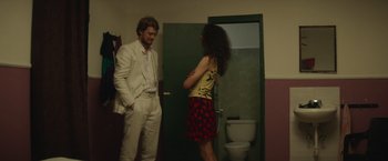Movie still from “Stars at Noon” (2022), directed by Claire Denis – A man and a woman standing in front of a toilet; Medium shot, Over the shoulder angle