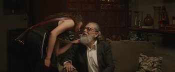 Movie still from “Stars at Noon” (2022), directed by Claire Denis – An older man and a young woman are sitting on a couch; Medium shot, Over the shoulder angle