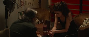 Movie still from “Stars at Noon” (2022), directed by Claire Denis – Two people sitting at a table with a glass of wine; Medium shot, High angle