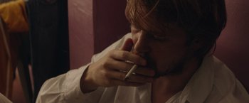 Movie still from “Stars at Noon” (2022), directed by Claire Denis – A man is smoking a cigarette in a room; Close Up shot, Over the shoulder angle