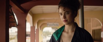 Movie still from “Stars at Noon” (2022), directed by Claire Denis – A young woman is standing in front of a building; Close Up shot, Low angle