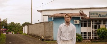 Movie still from “Stars at Noon” (2022), directed by Claire Denis – A man standing in front of a brick building; Medium shot, Low angle