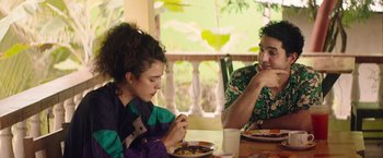 Movie still from “Stars at Noon” (2022), directed by Claire Denis – A man and a woman sitting at a table eating food; Medium shot, Over the shoulder angle