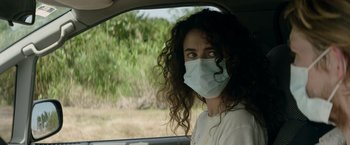 Movie still from “Stars at Noon” (2022), directed by Claire Denis – A woman wearing a face mask in a car; Close Up shot, Over the shoulder angle