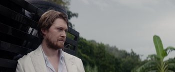 Movie still from “Stars at Noon” (2022), directed by Claire Denis – A man in a white suit is standing in front of a bench; Close Up shot, Low angle