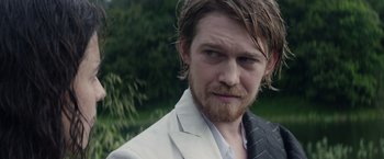 Movie still from “Stars at Noon” (2022), directed by Claire Denis – A person wearing a suit and beard; Close Up shot, Over the shoulder angle