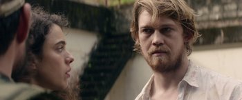 Movie still from “Stars at Noon” (2022), directed by Claire Denis – A man with a long beard standing next to a woman; Close Up shot, Over the shoulder angle