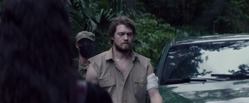 Movie still from “Stars at Noon” (2022), directed by Claire Denis – A man with a bandage on his arm is standing next to a car; Medium shot, Over the shoulder angle