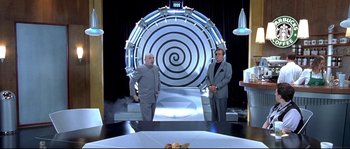 Movie still from “Austin Powers: The Spy Who Shagged Me” (1999), directed by Jay Roach – Two men standing in front of a spiral wall in a room; Wide shot, High angle