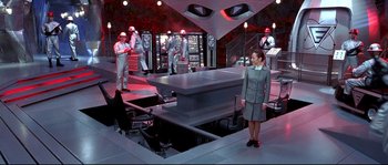 Movie still from “Austin Powers: The Spy Who Shagged Me” (1999), directed by Jay Roach – A woman standing in front of a table in a room; Wide shot, High angle