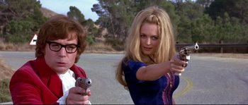 Movie still from “Austin Powers: The Spy Who Shagged Me” (1999), directed by Jay Roach – A woman holding a gun and pointing at a man; Medium shot, Low angle