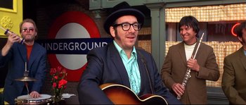 Movie still from “Austin Powers: The Spy Who Shagged Me” (1999), directed by Jay Roach – A man in a suit and hat is playing a guitar; Medium shot, Over the shoulder angle