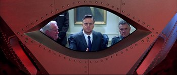 Movie still from “Austin Powers: The Spy Who Shagged Me” (1999), directed by Jay Roach – A man in a suit sitting in front of two other men; Medium shot, Over the shoulder angle