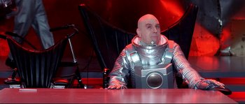 Movie still from “Austin Powers: The Spy Who Shagged Me” (1999), directed by Jay Roach – A man in a space suit sitting at a table; Medium shot, Low angle