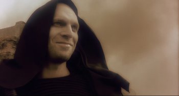 Movie still from “Avalon” (2001), directed by Mamoru Oshii – A man wearing a black robe and a black hood; Close Up shot, Low angle