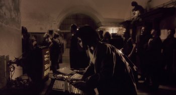 Movie still from “Avalon” (2001), directed by Mamoru Oshii – A group of people standing around a room with computers on it; Wide shot, High angle