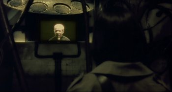 Movie still from “Avalon” (2001), directed by Mamoru Oshii – A person watching a television screen with an old man on it; Close Up shot, Over the shoulder angle