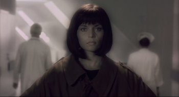 Movie still from “Avalon” (2001), directed by Mamoru Oshii – A woman in a brown coat is looking at the camera; Close Up shot, Low angle