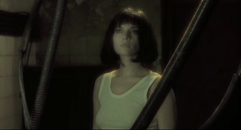 Movie still from “Avalon” (2001), directed by Mamoru Oshii – A woman in a white tank top is standing in front of a metal pole; Close Up shot, Low angle