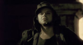 Movie still from “Avalon” (2001), directed by Mamoru Oshii – A man wearing a hat and holding a microphone; Close Up shot, Low angle