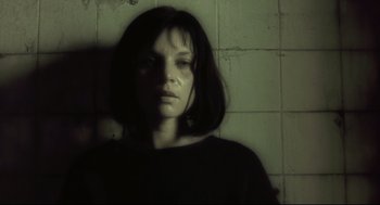 Movie still from “Avalon” (2001), directed by Mamoru Oshii – A woman is standing against a brick wall; Close Up shot, Low angle