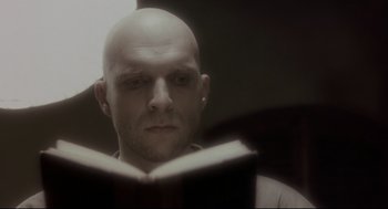 Movie still from “Avalon” (2001), directed by Mamoru Oshii – A bald man reading a book in a dark room; Close Up shot, Low angle