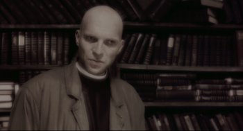Movie still from “Avalon” (2001), directed by Mamoru Oshii – A man with a priest's collar standing in front of a book shelf; Close Up shot, Low angle