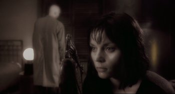 Movie still from “Avalon” (2001), directed by Mamoru Oshii – A woman is looking at the camera while a man stands in the background; Close Up shot, Low angle