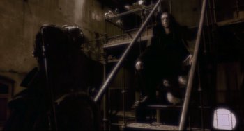 Movie still from “Avalon” (2001), directed by Mamoru Oshii – An image of a man sitting on a chair in a dark room; Wide shot, Low angle