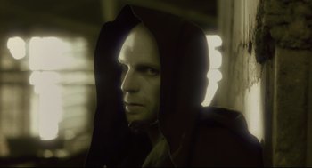 Movie still from “Avalon” (2001), directed by Mamoru Oshii – A man wearing a hooded jacket in a dark room; Close Up shot, Low angle
