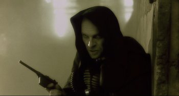 Movie still from “Avalon” (2001), directed by Mamoru Oshii – A man in a black hooded jacket holding a gun; Close Up shot, Low angle