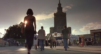 Movie still from “Avalon” (2001), directed by Mamoru Oshii – A group of people walking down a sidewalk near a tall building; Wide shot, Low angle