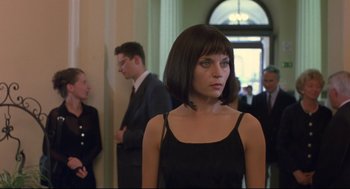 Movie still from “Avalon” (2001), directed by Mamoru Oshii – A woman in a black dress standing in front of a group of people; Medium shot, Over the shoulder angle