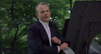 Movie still from “Avalon” (2001), directed by Mamoru Oshii – A man wearing a suit and tie sitting in front of trees; Close Up shot, Low angle