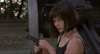 Movie still from “Avalon” (2001), directed by Mamoru Oshii – A woman holding a gun while standing next to a building; Close Up shot, Low angle