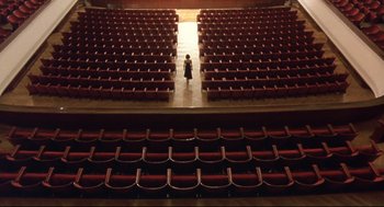 Movie still from “Avalon” (2001), directed by Mamoru Oshii – A person is standing in the middle of an auditorium; Extreme Wide shot, High angle