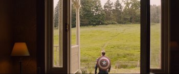 Movie still from “Avengers: Age of Ultron” (2015), directed by Joss Whedon – A man wearing a captain america's shield stands on the porch of a house; Extreme Wide shot, High angle
