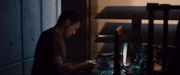 Movie still from “Avengers: Age of Ultron” (2015), directed by Joss Whedon – A man sitting in front of a computer at a desk; Medium shot, Over the shoulder angle
