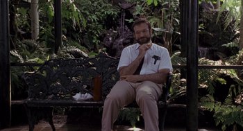 Movie still from “Awakenings” (1990), directed by Penny Marshall – A man sitting on top of a wooden bench in a garden; Wide shot, Low angle