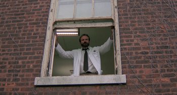 Movie still from “Awakenings” (1990), directed by Penny Marshall – A man in a white lab coat and tie standing in a window; Medium shot, Low angle