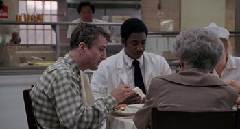 Movie still from “Awakenings” (1990), directed by Penny Marshall – A group of people sitting at a table eating food; Medium shot, Over the shoulder angle
