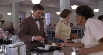 Movie still from “Awakenings” (1990), directed by Penny Marshall – A man in a brown suit and a woman in a yellow sweater are serving food; Medium shot, Over the shoulder angle