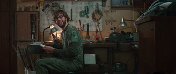 Movie still from “Away We Go” (2009), directed by Sam Mendes – A man sitting at a table in front of a work bench; Medium shot, Low angle