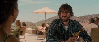 Movie still from “Away We Go” (2009), directed by Sam Mendes – A man sitting on top of a chair under an umbrella; Medium shot, Over the shoulder angle