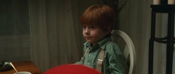 Movie still from “Away We Go” (2009), directed by Sam Mendes – A young boy sitting at a table looking at the camera; Close Up shot, Over the shoulder angle
