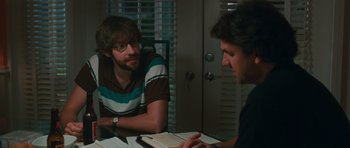 Movie still from “Away We Go” (2009), directed by Sam Mendes – Two men are sitting at a table and one is reading a book; Medium shot, Over the shoulder angle