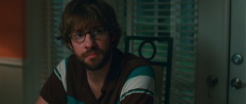Movie still from “Away We Go” (2009), directed by Sam Mendes – A man sitting in a chair wearing glasses; Close Up shot, Over the shoulder angle